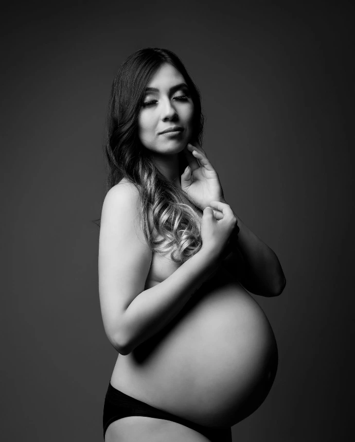 Fotografía artística de maternidad en blanco y negro con fondo oscuro.