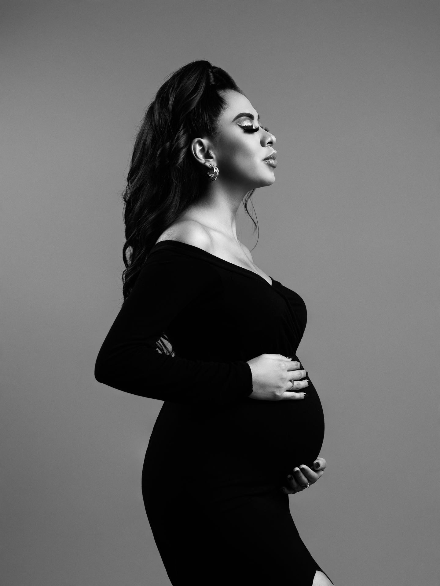 Fotografía de maternidad en perfil con vestido negro sobre fondo oscuro.