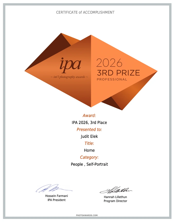 certificado de tercer lugar de IPA 2026 junto a una impresión del autorretrato Home de Judit Elek