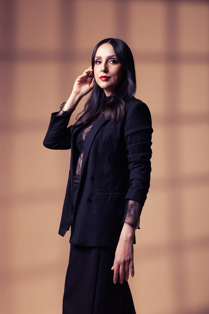 Retrato de mujer con saco oscuro y una mano cerca del rostro, frente a un fondo cálido en estudio fotográfico.