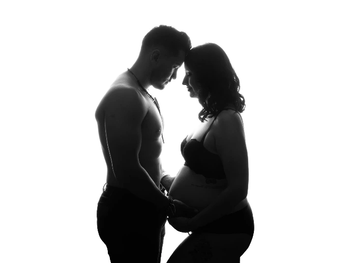 Retrato de embarazo en pareja con silueta iluminada en estudio.